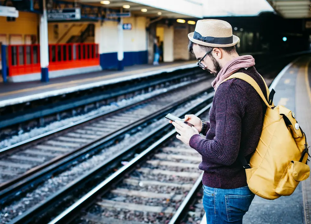 A traveller checking their phone on a train platform after landing abroad